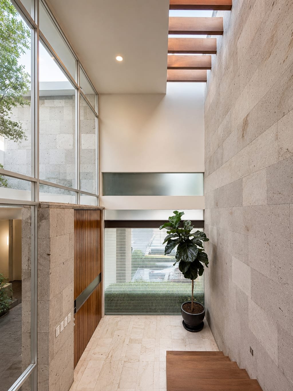 Vestíbulo de doble altura de Casa Quatro con muro de piedra y lucernario de vigas de madera